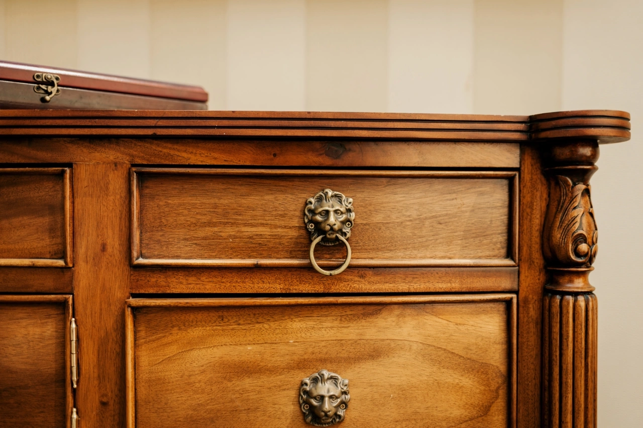 Close-up of a wooden dresser with ornate lion head drawer pulls and a partially visible box on top.